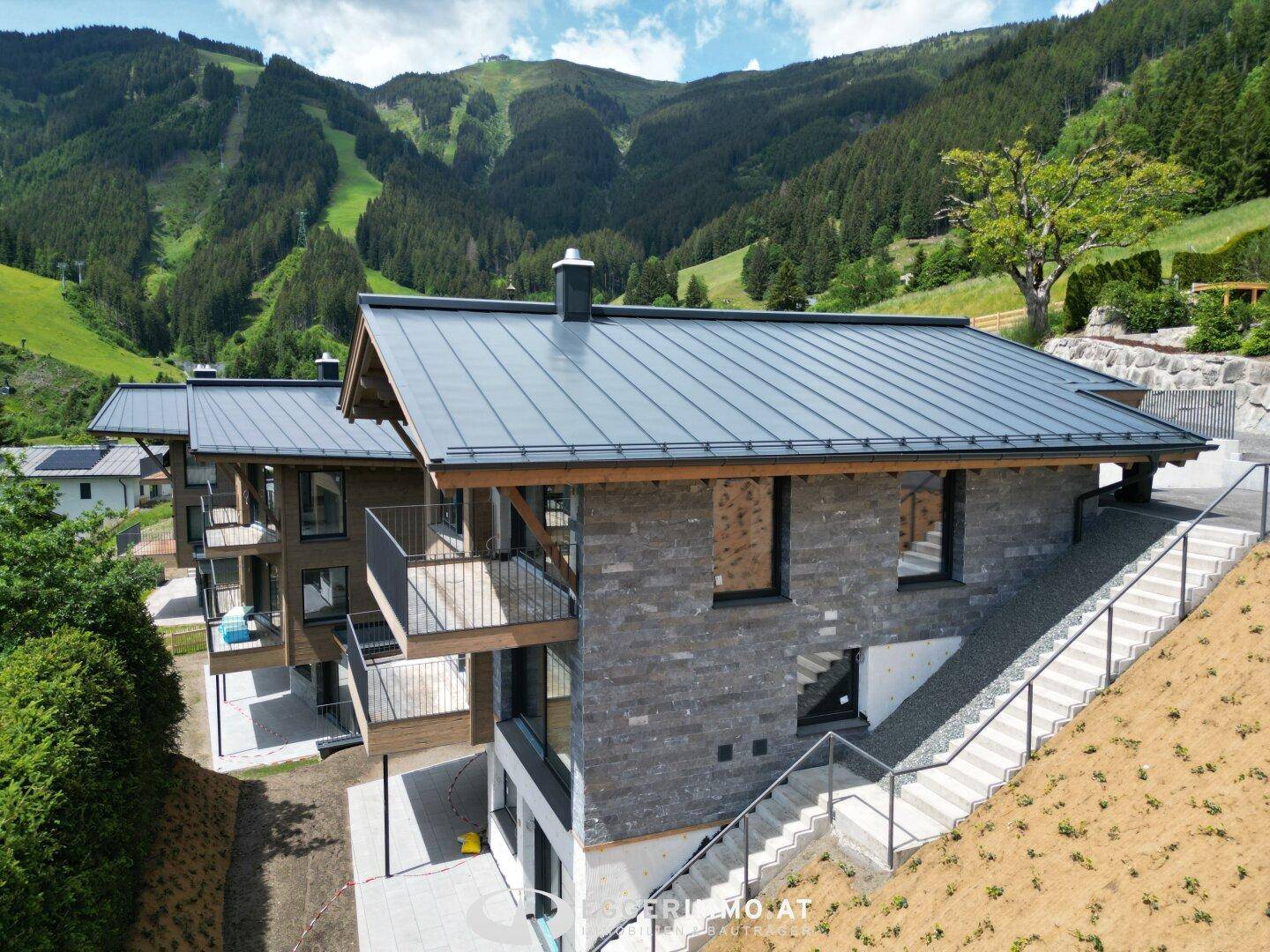 Modernes Chalet mit Steinfassade und Balkonen, eingebettet in eine grüne Berglandschaft.