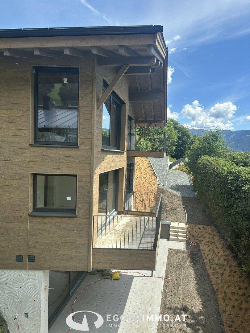 Seitenansicht eines modernen Holzchalets mit Balkonen und Blick auf die Umgebung.