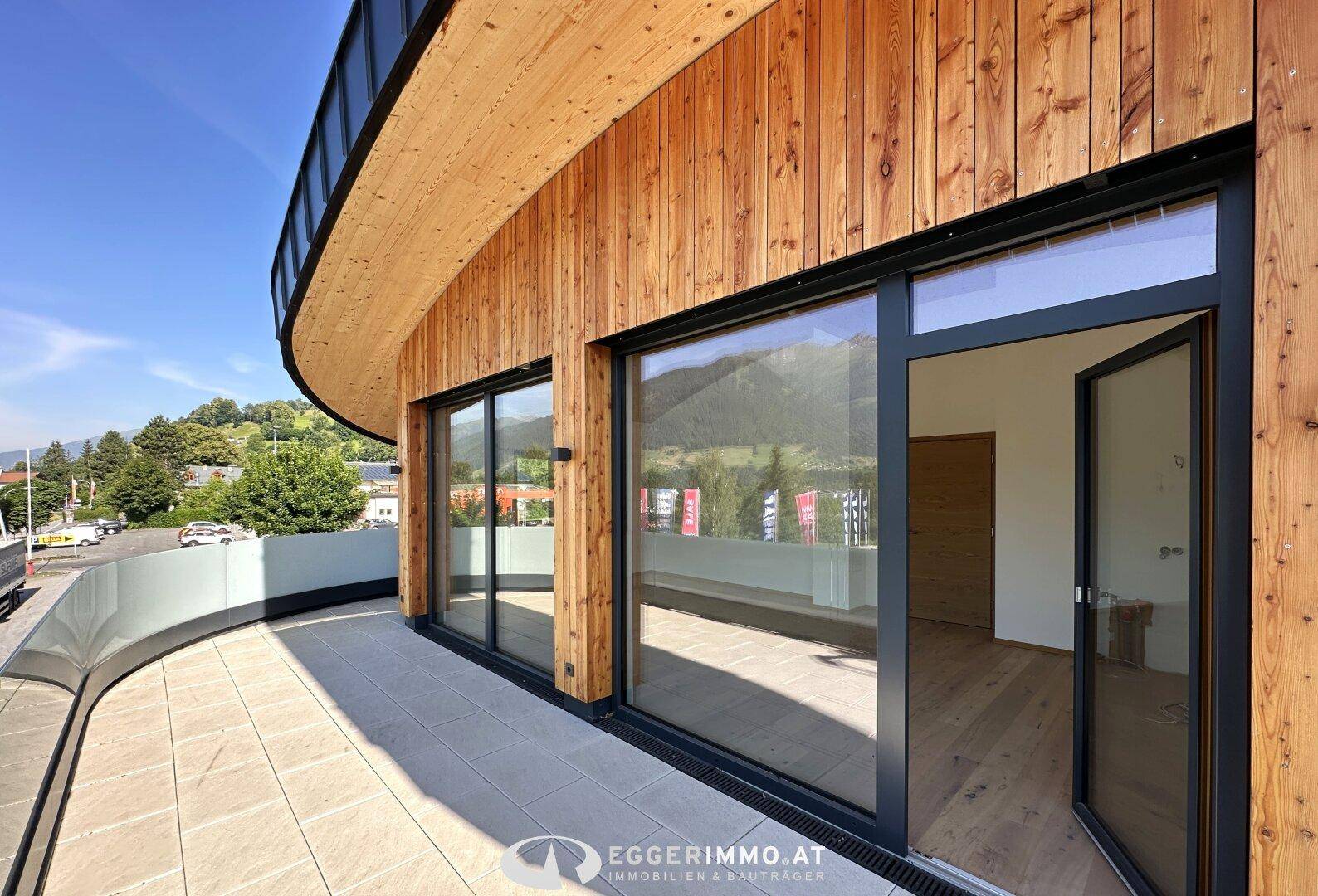 Moderne Terrasse mit Holzfassade, Glasgeländer und weitem Blick auf die umliegende Berglandschaft.