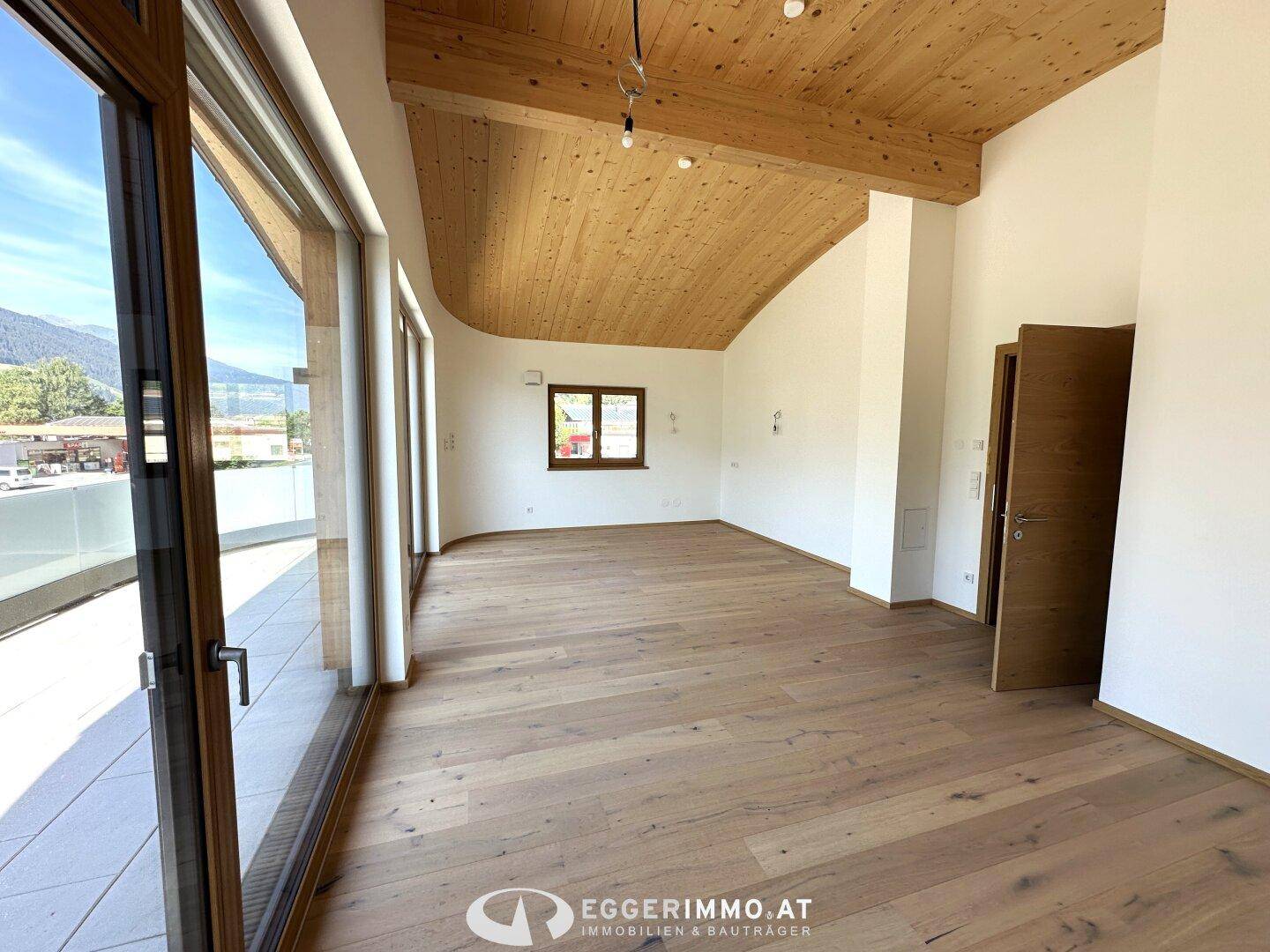 Geräumiger Wohnbereich mit Holzboden, Holzdecke und einem Fenster mit Blick auf die Natur.