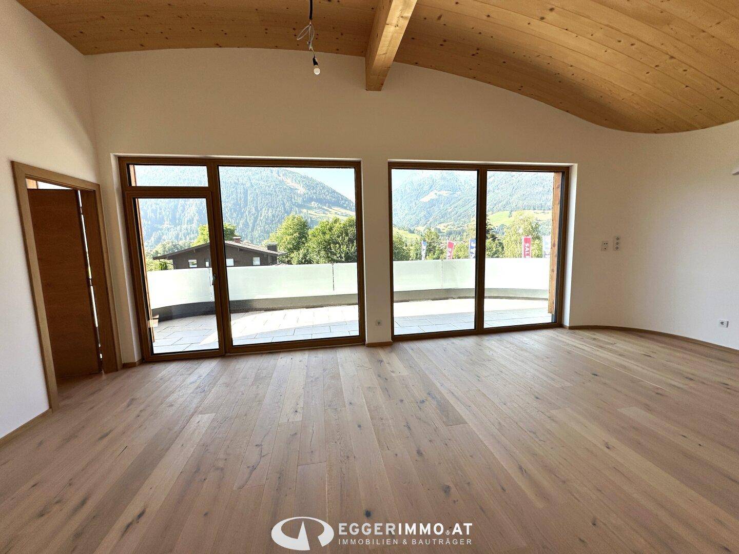 Heller Wohnraum mit Holzboden, Holzdecke und großen Fenstern, die einen weiten Bergblick bieten.