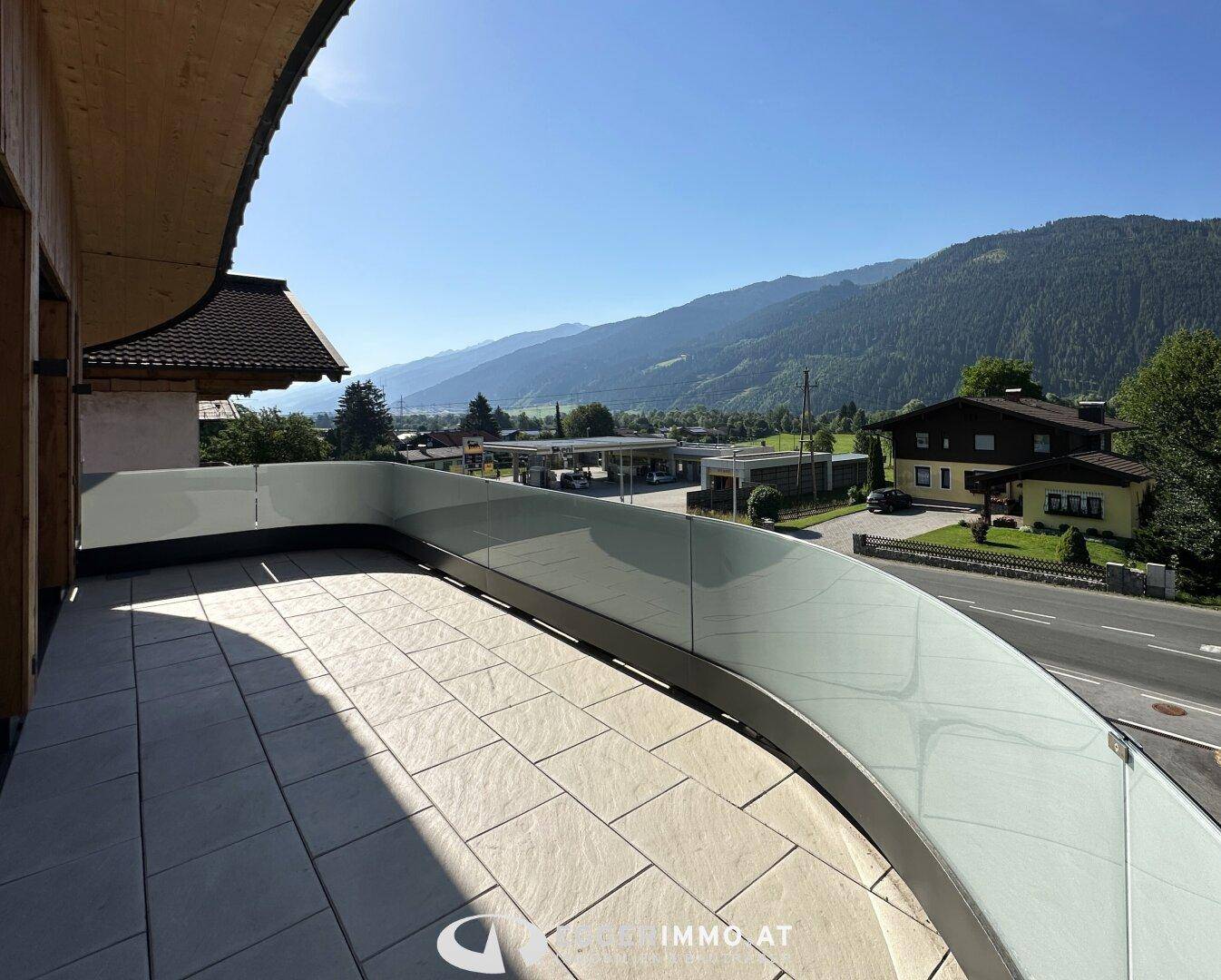 Geräumige Außenterrasse mit Fliesenboden, Glasgeländer und weitem Blick auf die Berge.