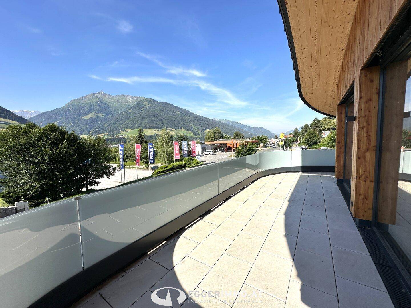 Sonniger Terrassenbereich mit Fliesenboden und Glasgeländer, umgeben von einer Berglandschaft.