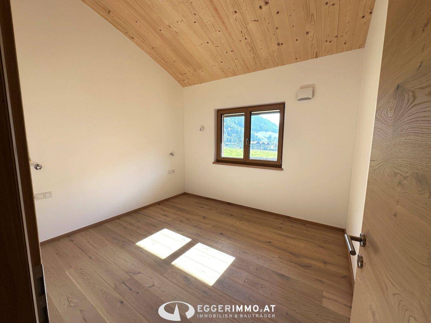 Gemütliches Schlafzimmer mit Holzboden und Fenster, das viel Tageslicht hereinlässt.