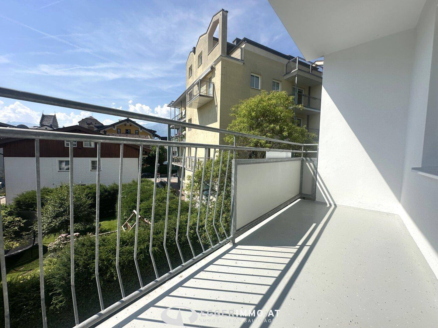 Heller Balkon mit Metallgeländer und Blick auf umliegende Gebäude und Bäume.