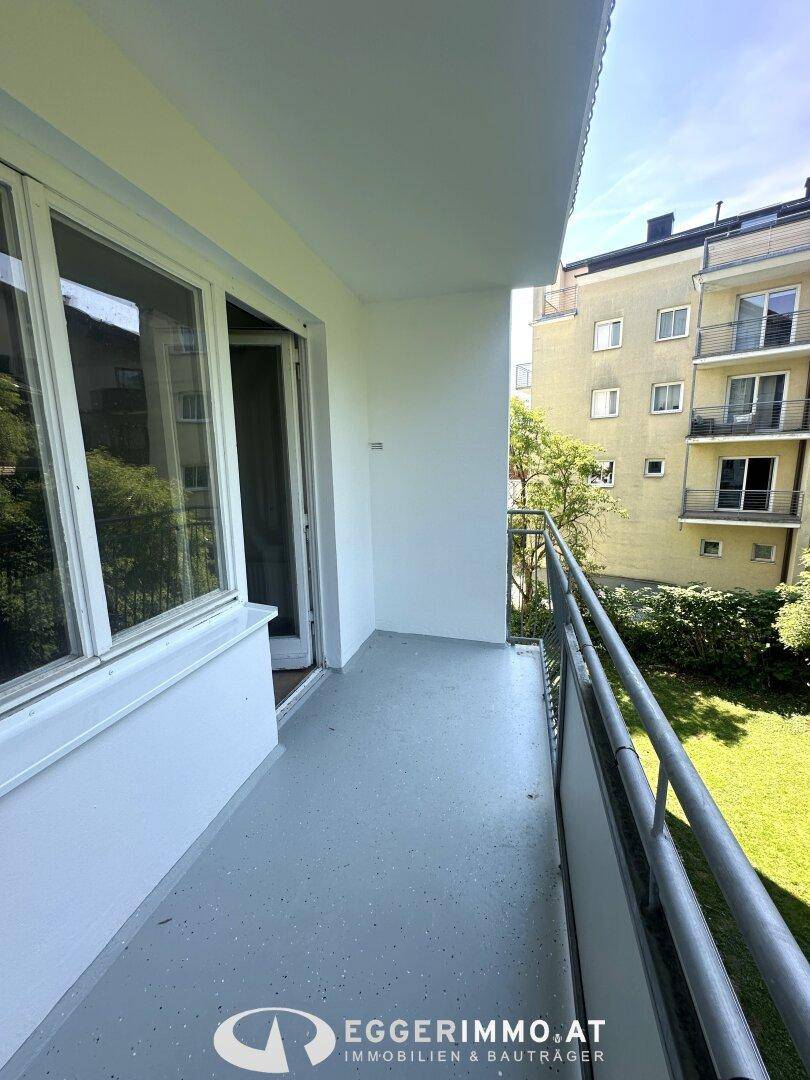 Heller Balkon mit grauem Boden und Blick auf einen grünen Rasen und Nachbargebäude.