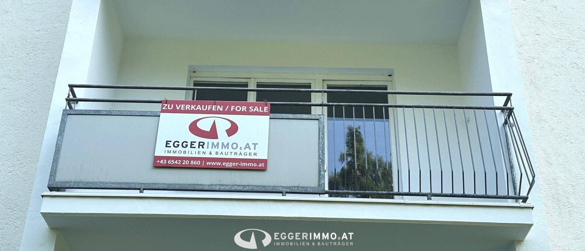 Nahaufnahme eines Balkons mit Metallgeländer und einem "Zu Verkaufen" Schild.