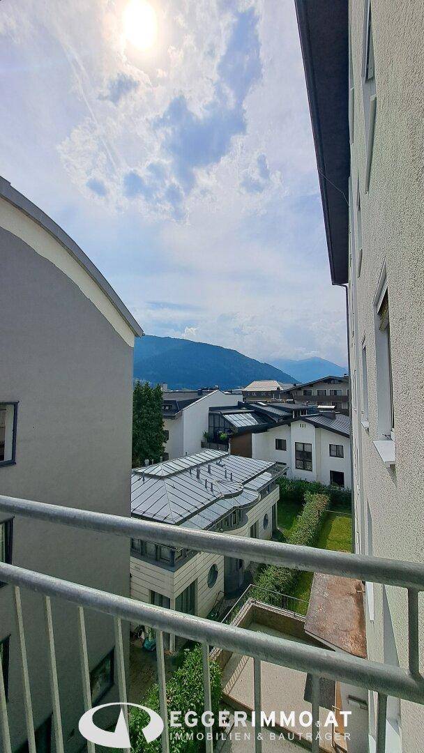 Aussicht vom Balkon auf benachbarte Gebäude und die malerische Bergkulisse unter einem sonnigen Himmel.