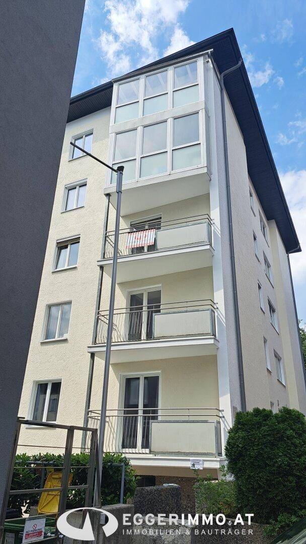 Mehrstöckiges Wohngebäude mit mehreren Balkonen und einem verglasten Wintergarten an der Fassade.