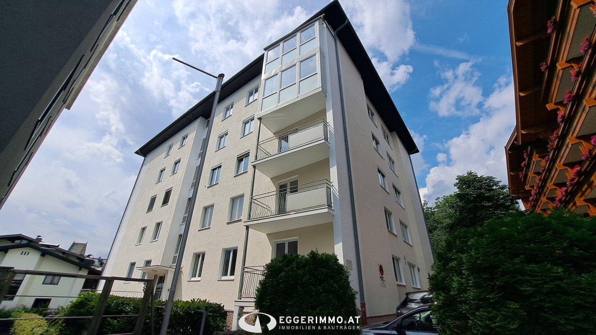 Ansicht des modernen Wohngebäudes mit seinen Balkonen und dem verglasten Anbau unter blauem Himmel.