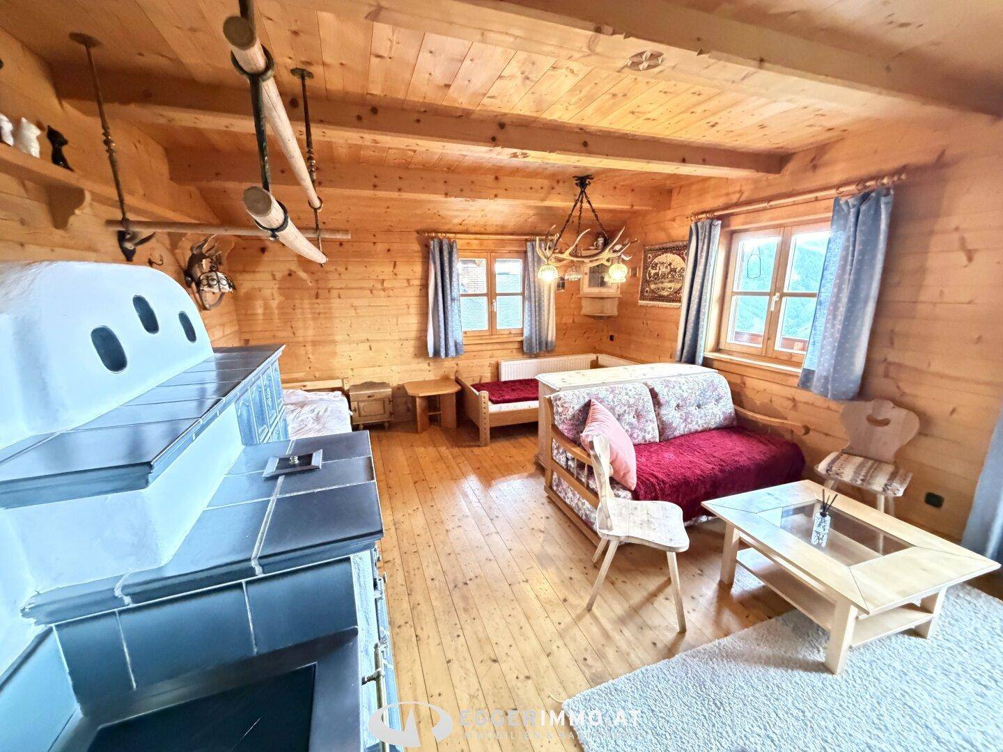 Gemütlicher Wohnbereich im alpenländischen Stil mit Holzwänden, Kachelofen und rustikalen Möbeln.