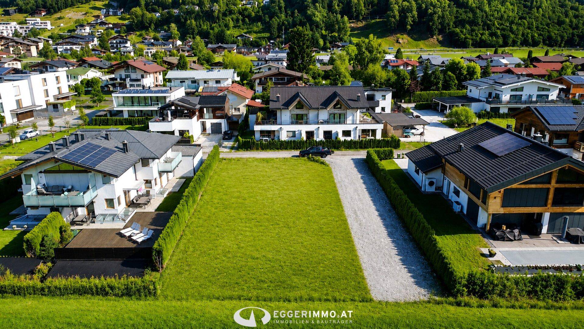 Luftaufnahme eines Baugrundstücks in einer Wohnsiedlung mit modernen Häusern und Bergblick.