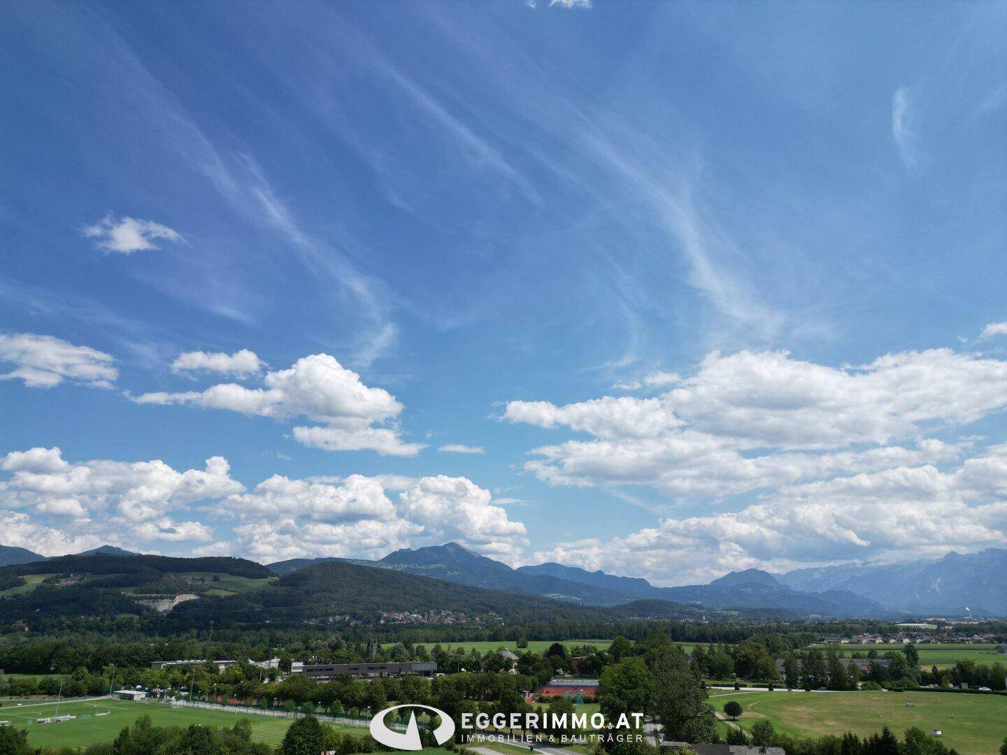 Weitläufiger Panoramablick über grüne Hügel und eine beeindruckende Bergkette unter blauem Himmel.