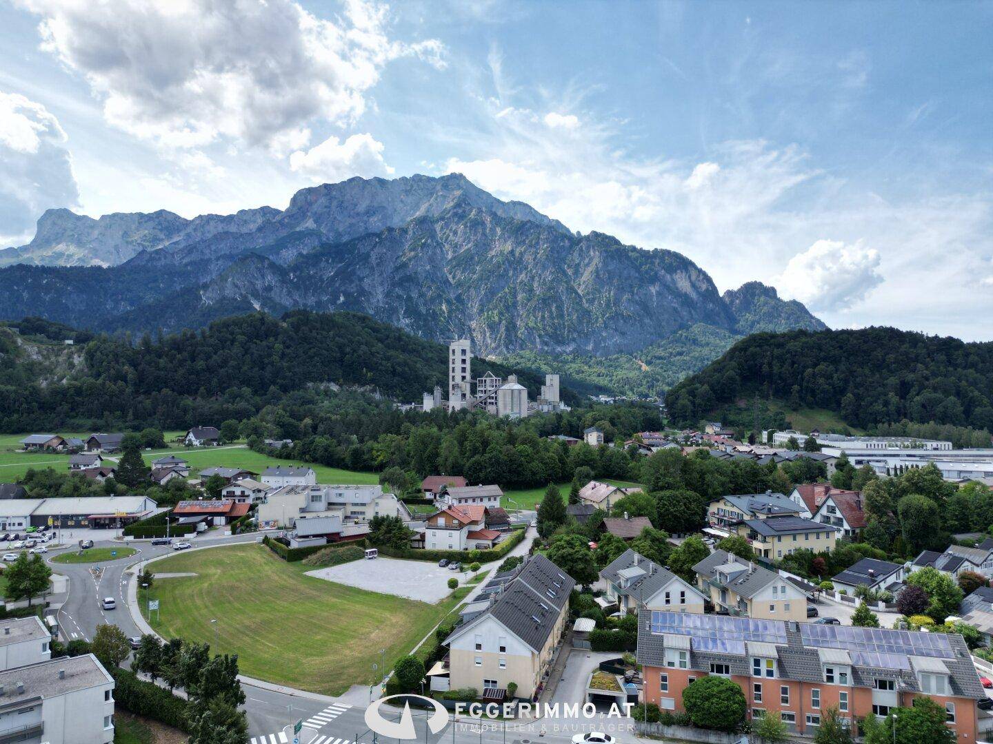 Luftaufnahme einer Siedlung am Fuße majestätischer Berge mit einer Industrieanlage im Hintergrund.
