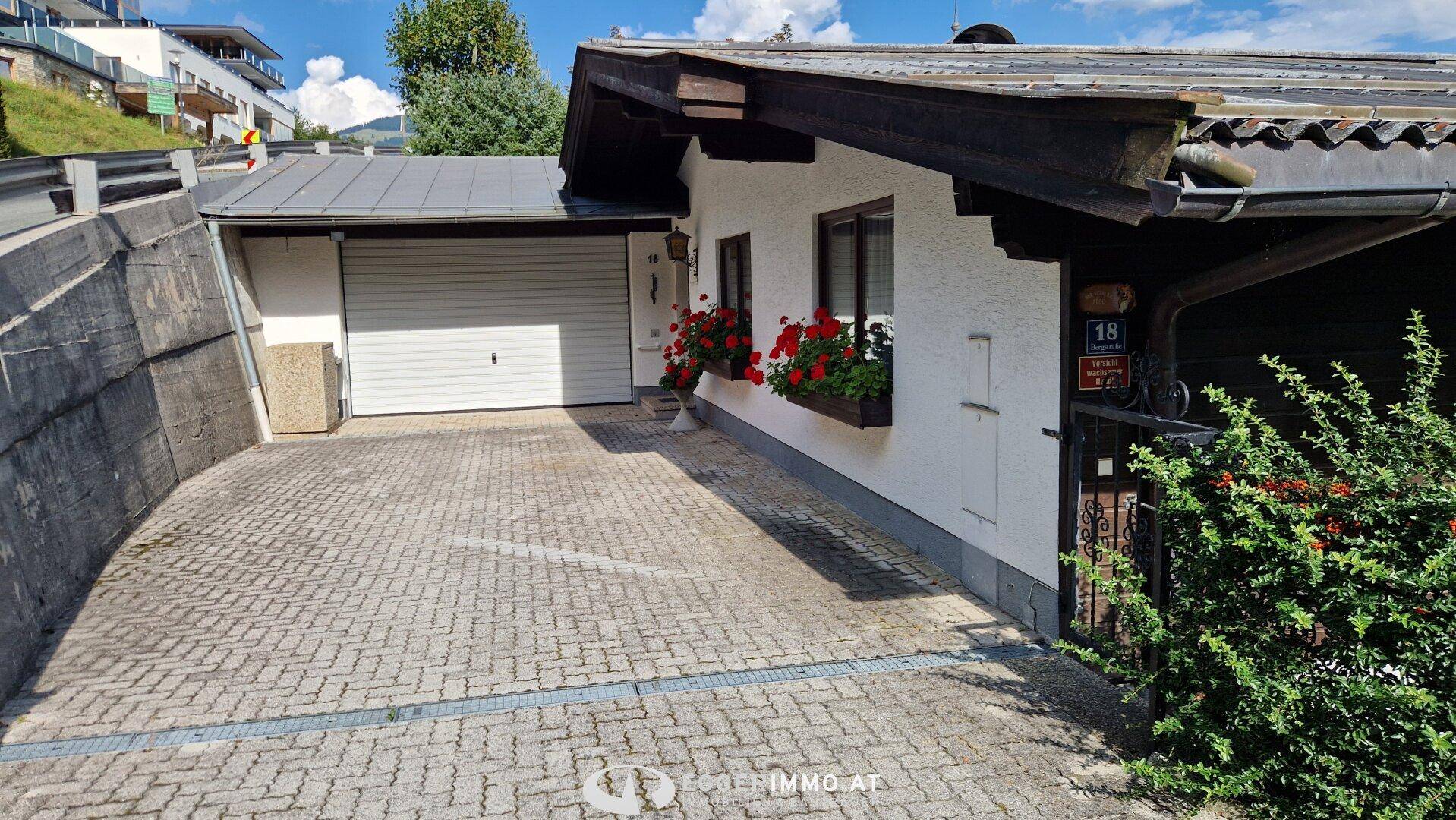 Einfahrt mit Pflastersteinen und einer Garage neben dem Haus mit Blumenkästen.