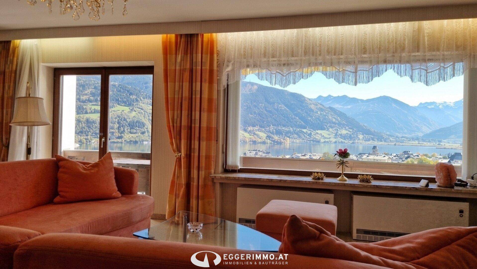Gemütliches Wohnzimmer mit orangefarbenen Sofas und einem weiten Blick auf den See und die Berge.