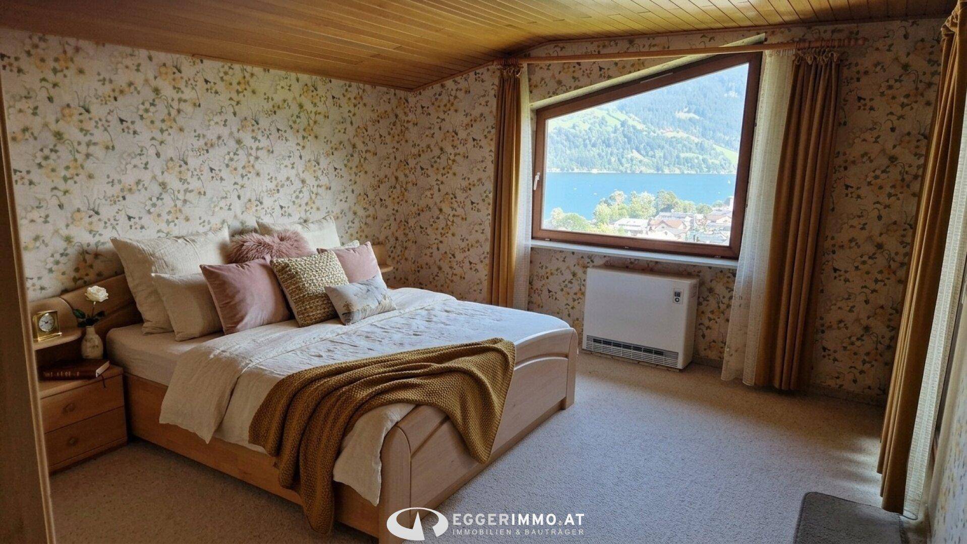 Schlafzimmer mit floraler Tapete, Holzbalkendecke und einem Fenster mit Seeblick.