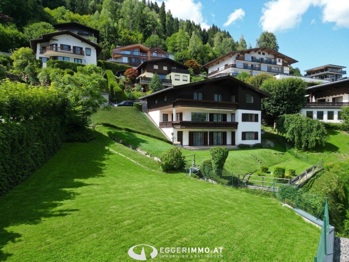 Großzügige grüne Rasenfläche vor dem Haus am Hang mit weiteren Gebäuden im Hintergrund.