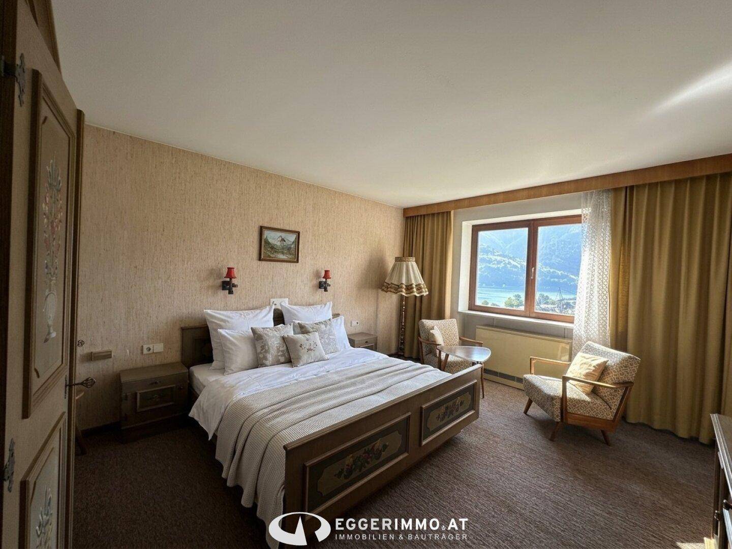 Geräumiges Schlafzimmer mit Doppelbett, Sitzgelegenheiten und malerischem Blick auf den See.