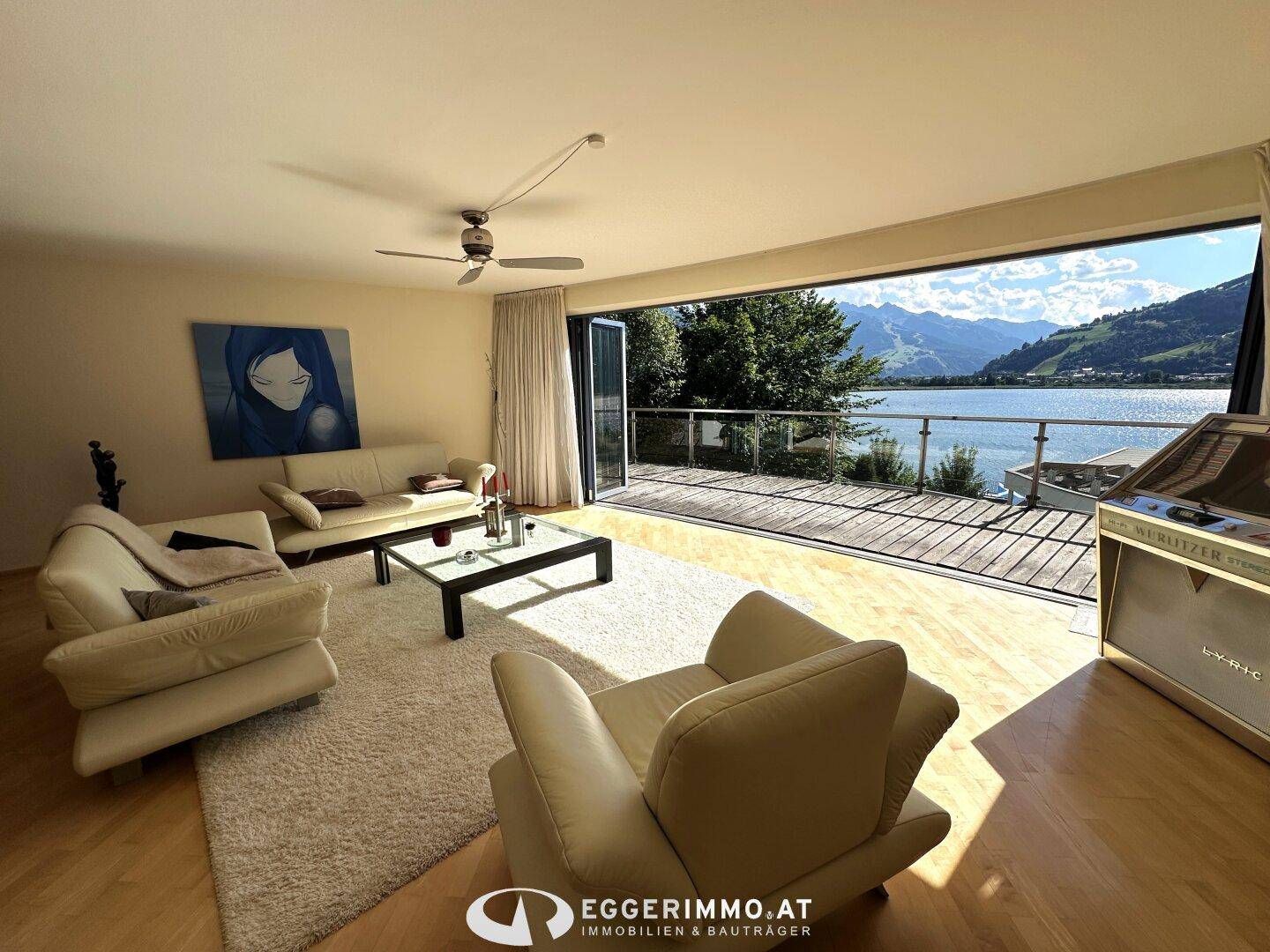 Helles Wohnzimmer mit großen Fenstern, die sich zu einer Terrasse mit See- und Bergblick öffnen.