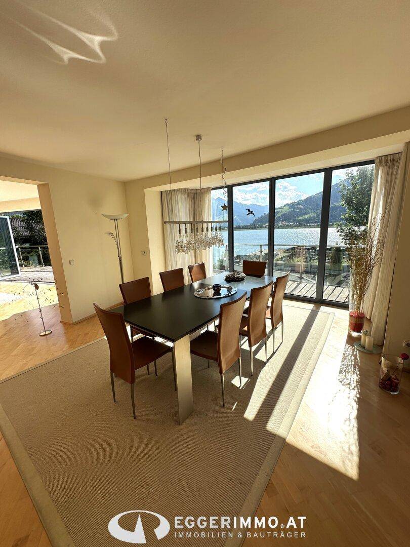 Heller Essbereich mit großem Tisch und Stühlen, bietet einen herrlichen Blick auf den See und die Berge.