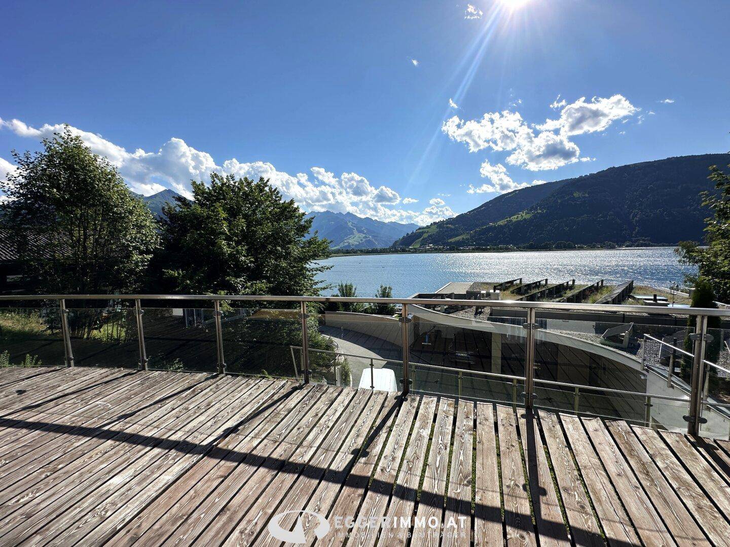 Geräumige Holzterrasse mit Glasgeländer bietet einen atemberaubenden Blick auf den See und die umliegenden Berge.