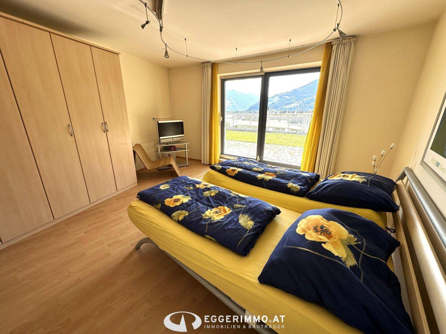 Schlafzimmer mit zwei Betten, Einbauschränken und großen Fenstern mit Bergblick.
