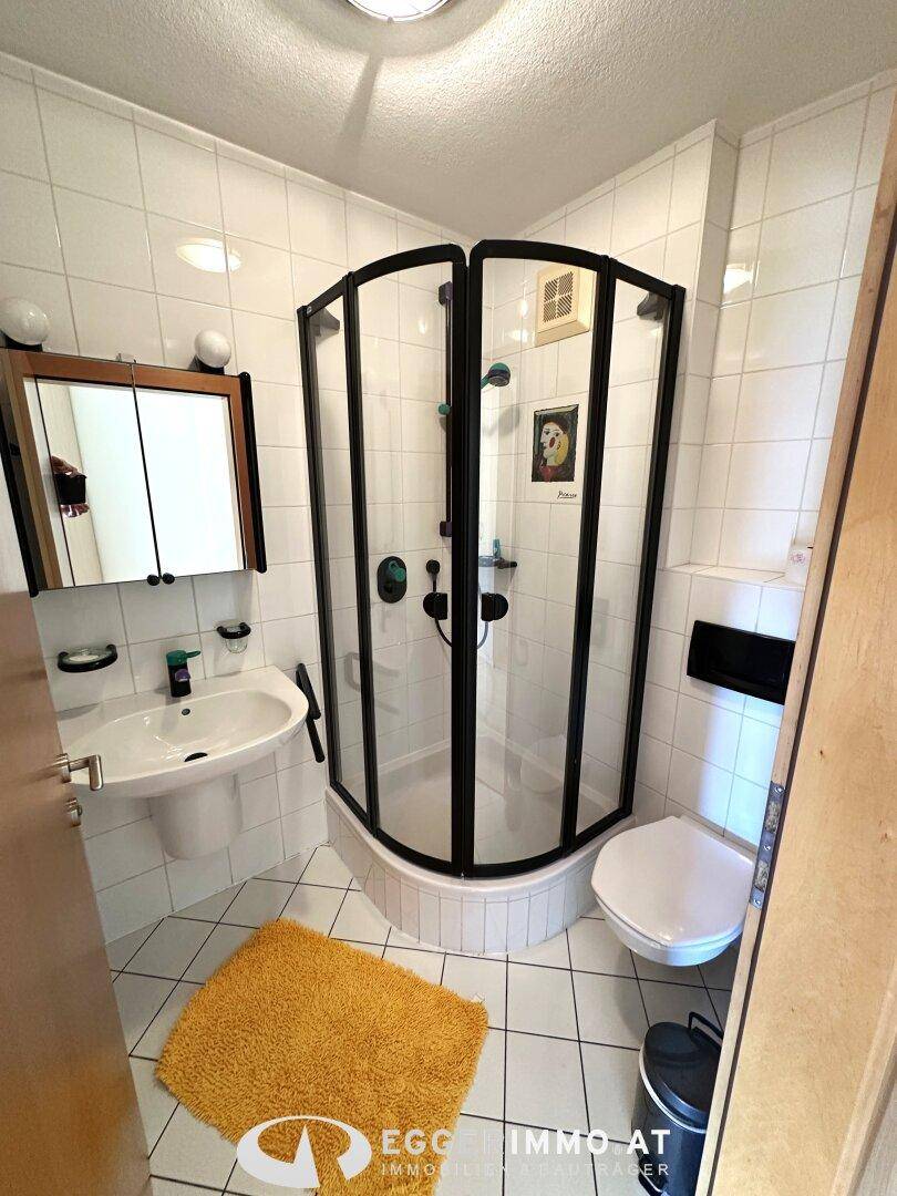 Kleines Badezimmer mit Duschkabine, WC und Waschbecken, ausgestattet mit weißen Fliesen.