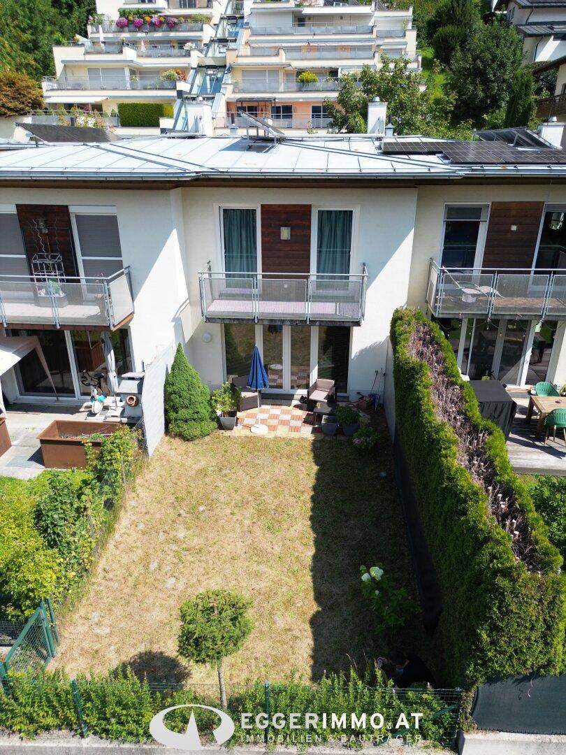 Gartenbereich mit Rasenfläche und kleiner Terrasse vor dem Haus, umgeben von Hecken.