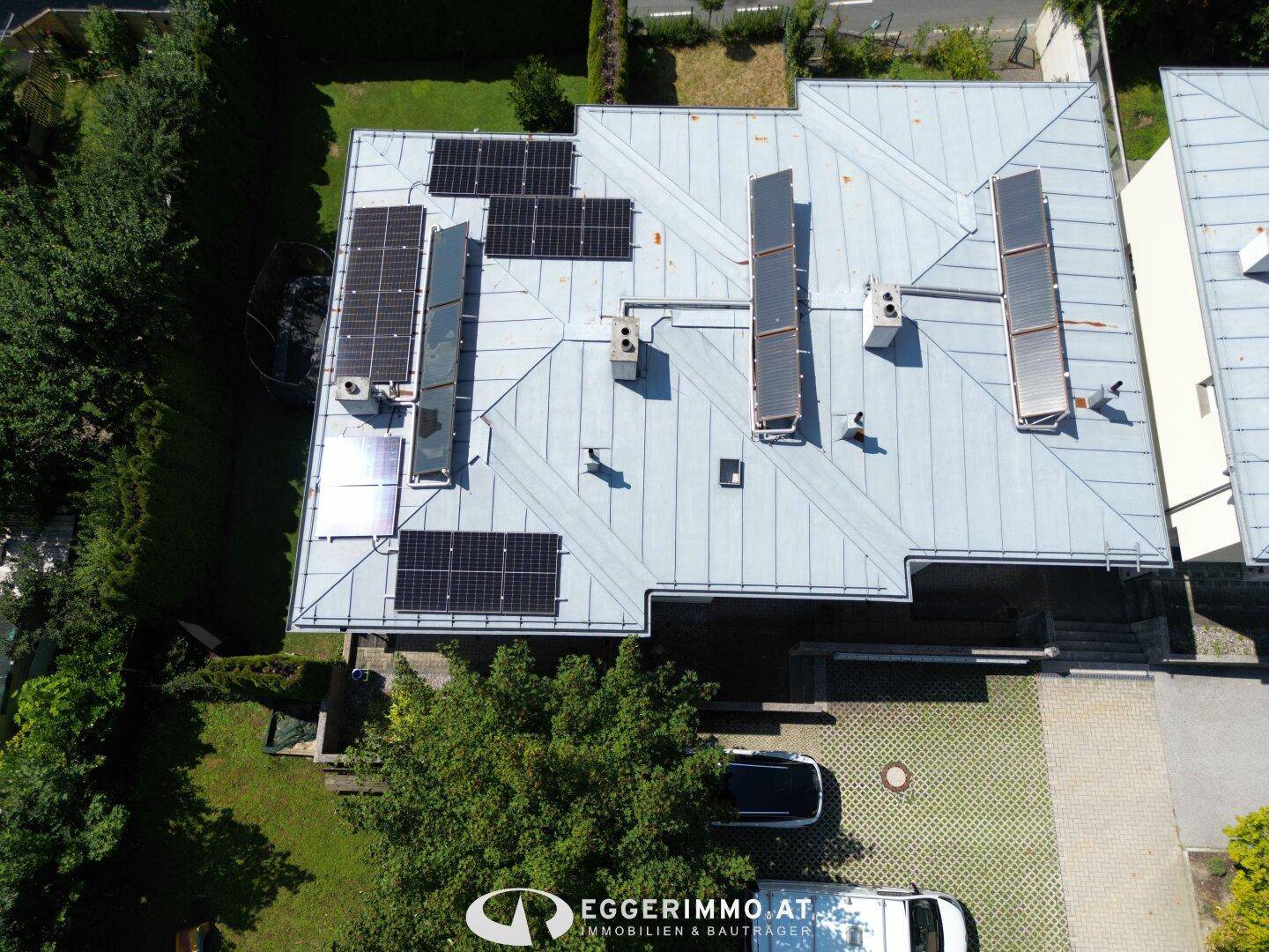 Dachansicht des Hauses mit mehreren Solaranlagen und einem gepflasterten Parkplatz.