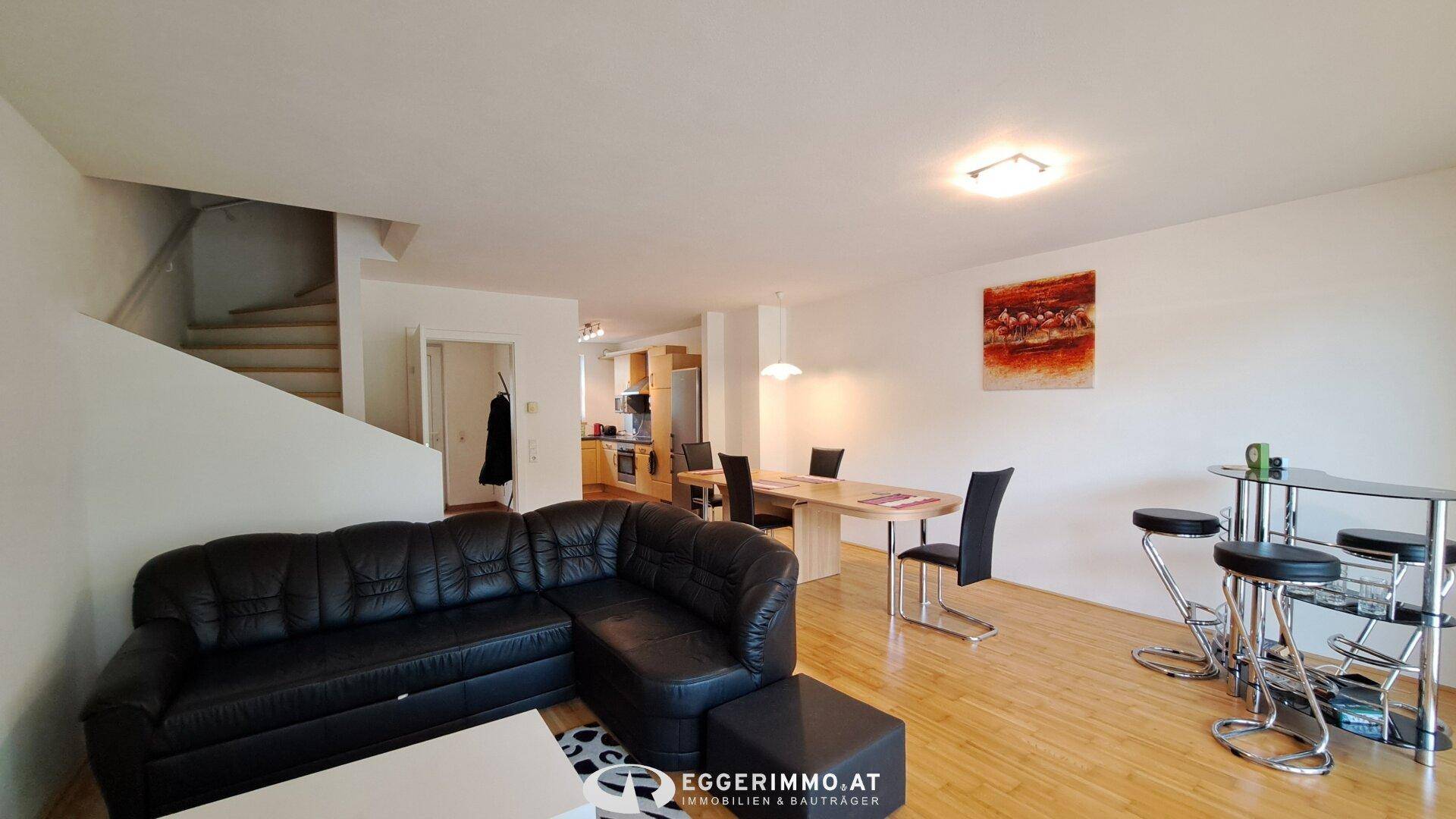 Geräumiger Wohn-Essbereich mit dunklem Ledersofa, Esstisch und Holzfußboden.