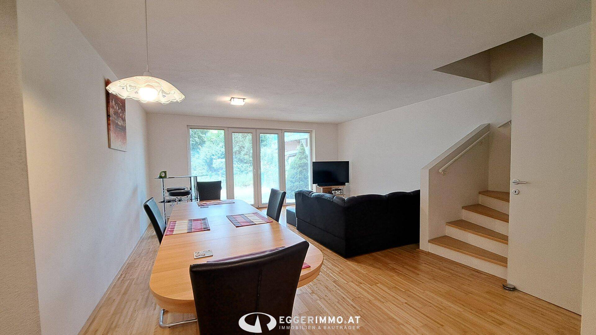 Offener Wohn-Essbereich mit großem Esstisch, Sofa und Zugang zur Terrasse durch große Fenster.