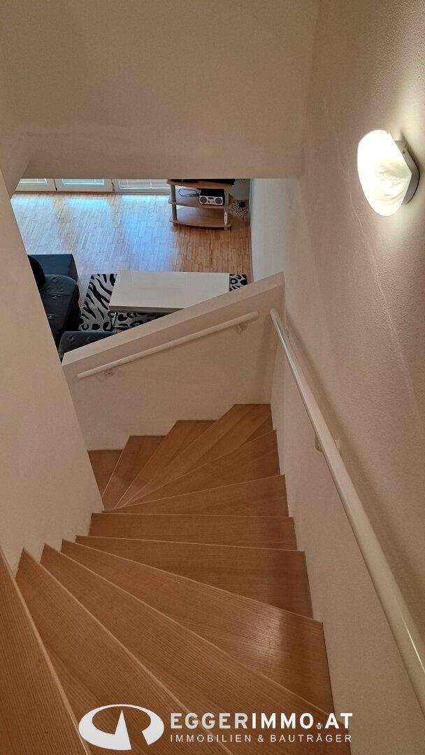 Holztreppe führt vom Wohnbereich in die obere Etage, hell beleuchtet.