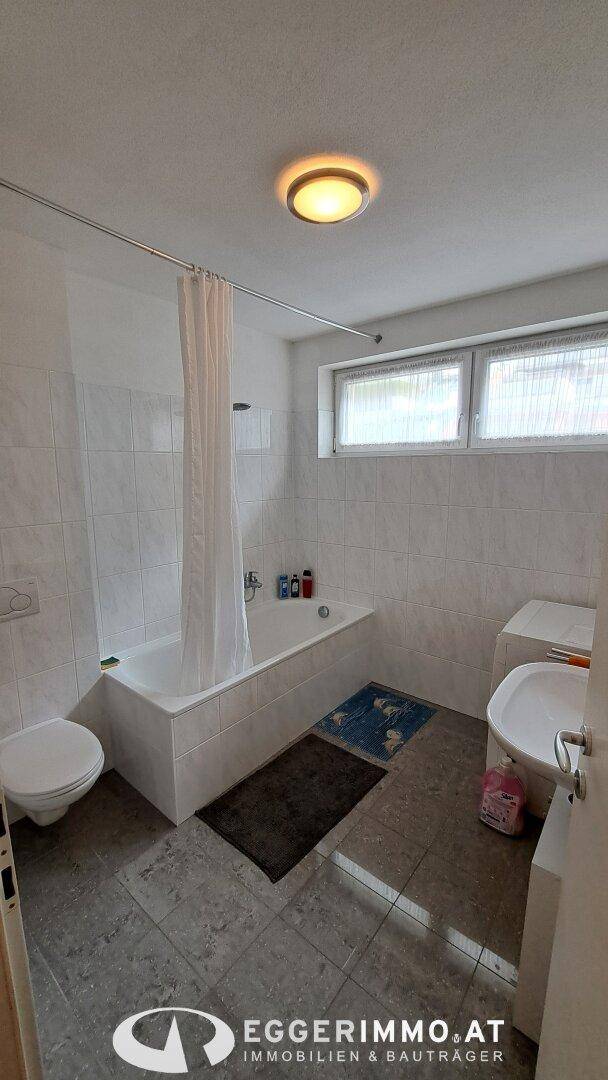 Badezimmer mit Badewanne, WC, Waschbecken und Fenster, ausgestattet mit hellen Fliesen.