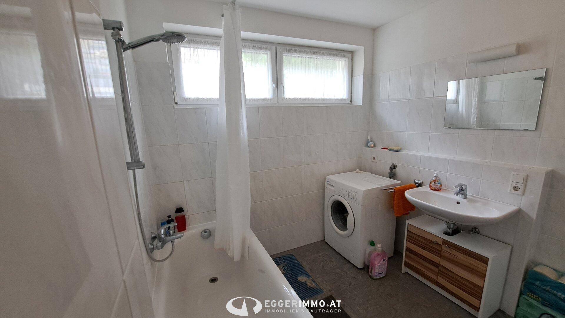 Helles Badezimmer mit Badewanne, Waschmaschine, Waschbecken und Spiegel, gefliest.