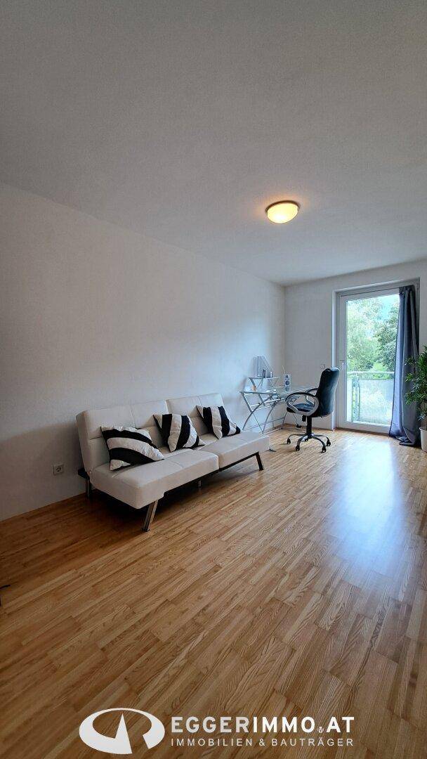 Helles Arbeitszimmer mit Sofa, Schreibtisch und Zugang zu einem Balkon durch eine Glastür.