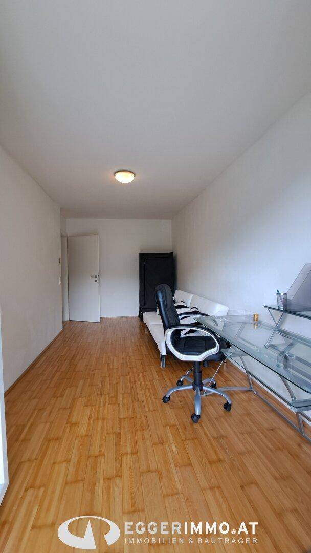 Arbeitszimmer mit Holzfußboden, Schreibtisch und Bürostuhl, minimalistisch eingerichtet.