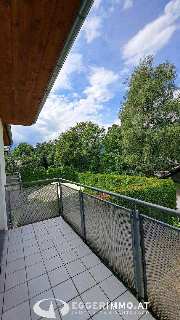 Balkon mit Fliesenboden und Metallgeländer, umgeben von grünen Bäumen und Hecken.