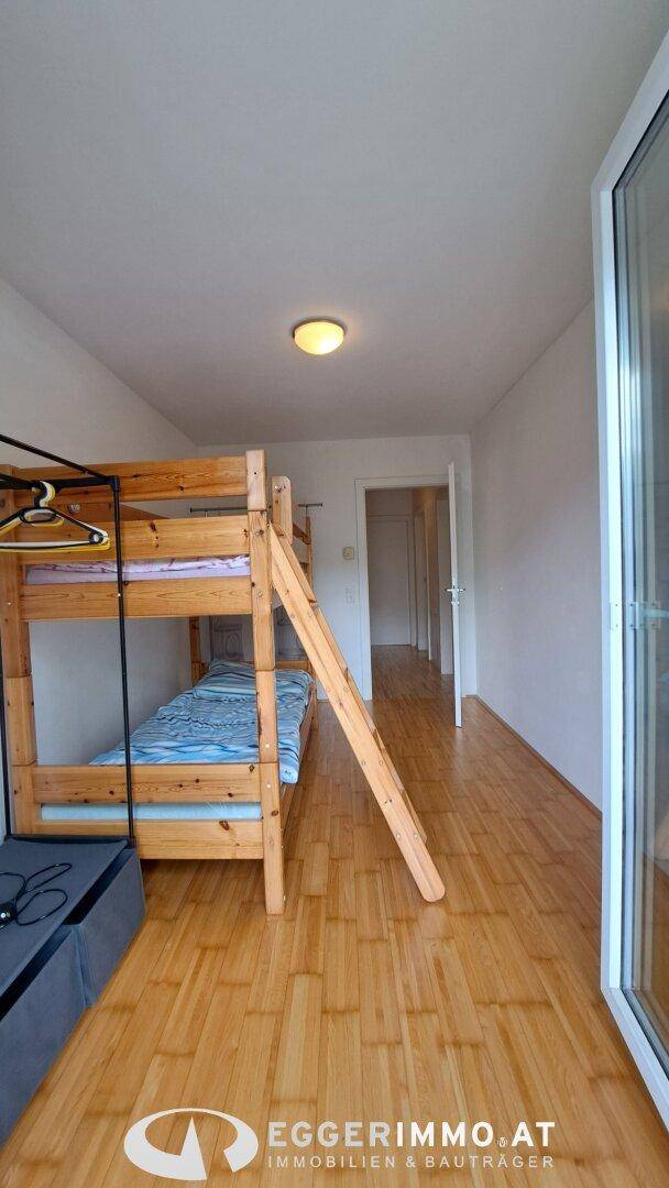Kinderzimmer mit Etagenbett, Holzfußboden und Zugang zu einem Balkon durch eine Glastür.