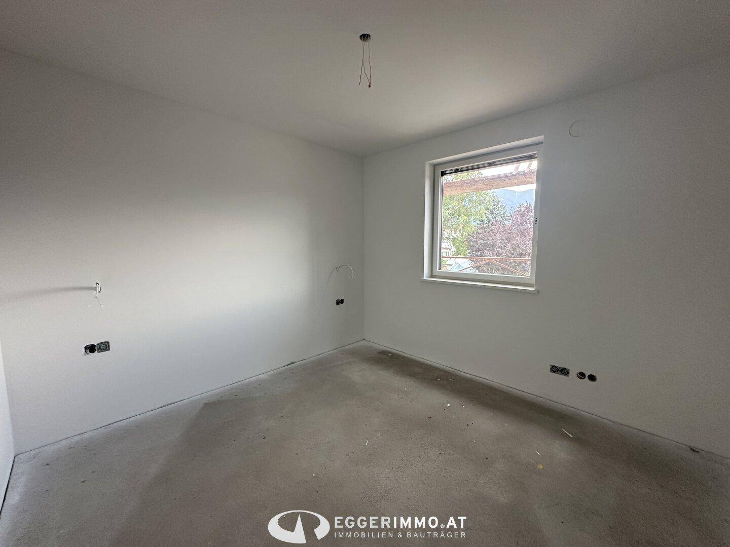 Unmöbliertes Schlafzimmer im Rohbau mit Betonboden und Fenster.