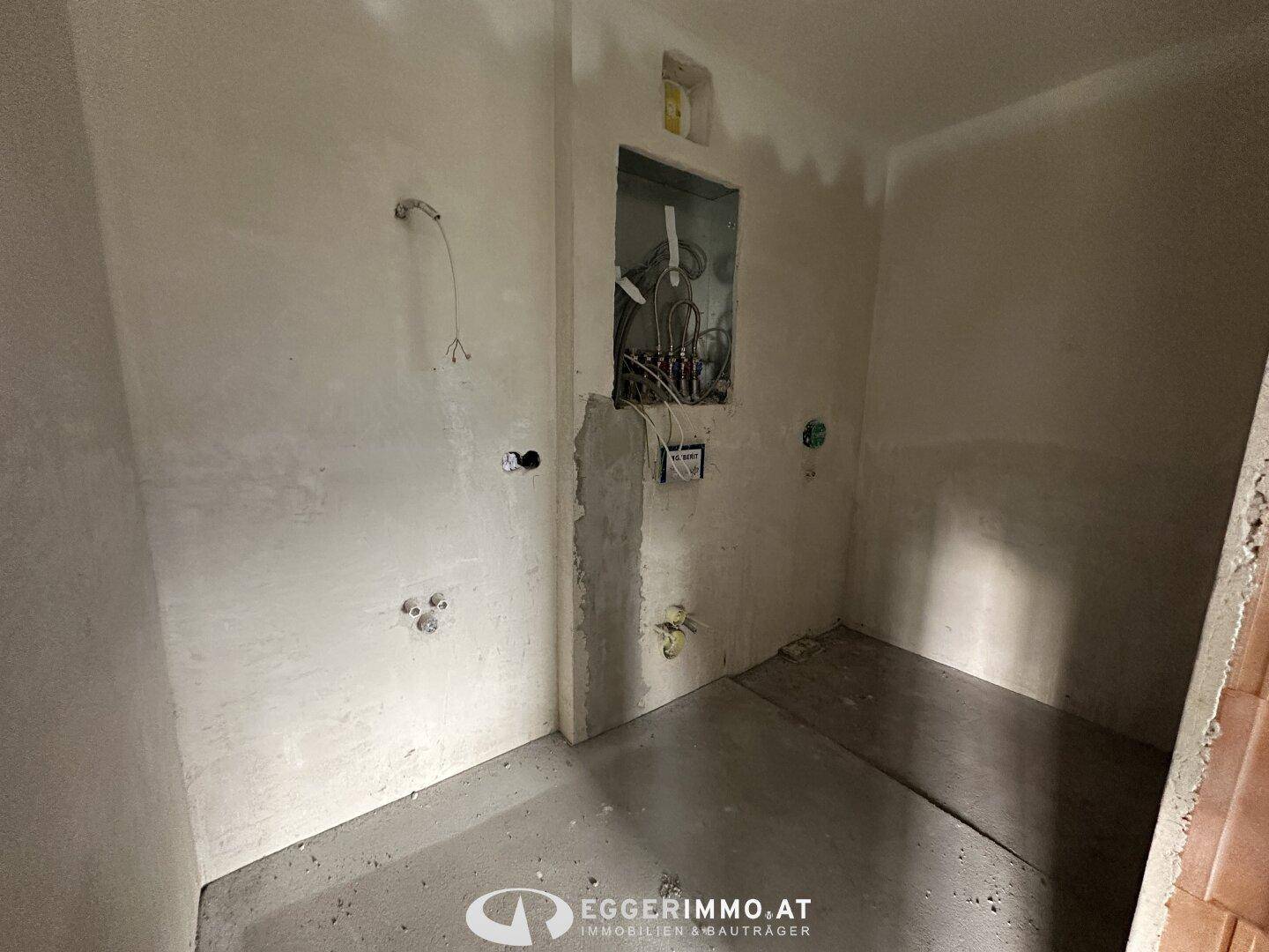 Unfertiges Badezimmer im Rohbau mit sichtbaren Installationen und Betonboden.