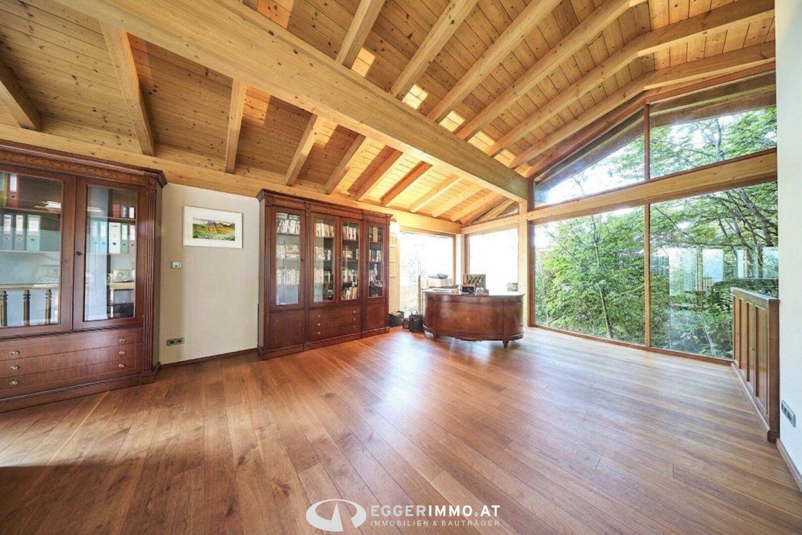 Helles Büro mit Holzbalkendecke, großen Fenstern und einem eleganten Schreibtisch mit Seeblick.