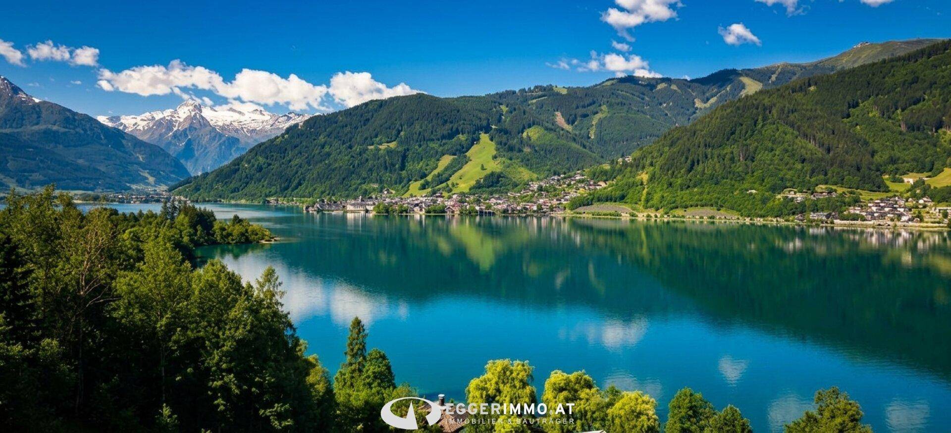 Panoramablick auf den malerischen See mit umliegenden Bergen und einer kleinen Ortschaft am Ufer.