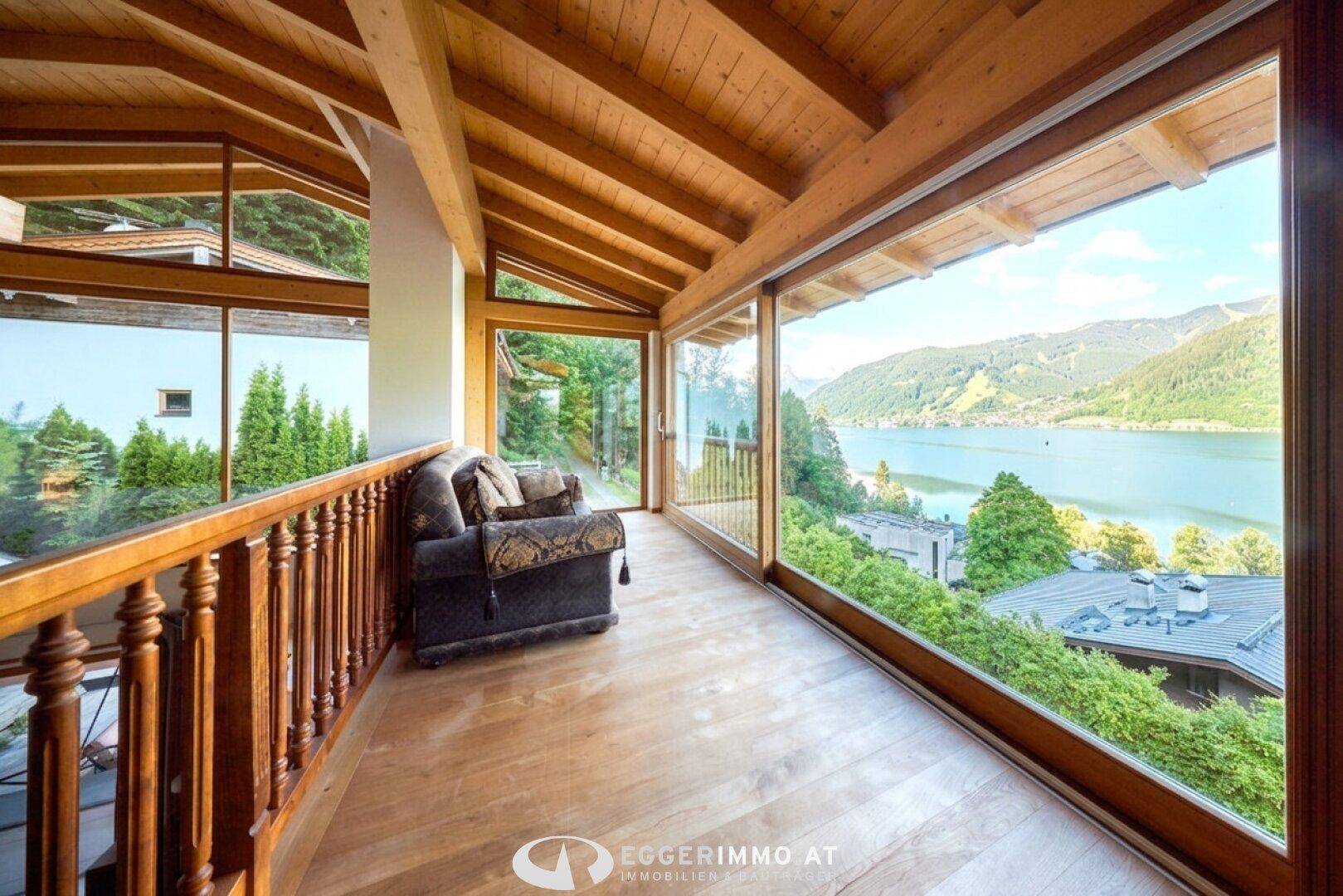 Gemütlicher verglaster Bereich mit Holzboden und Panoramablick auf den See und die Berge.