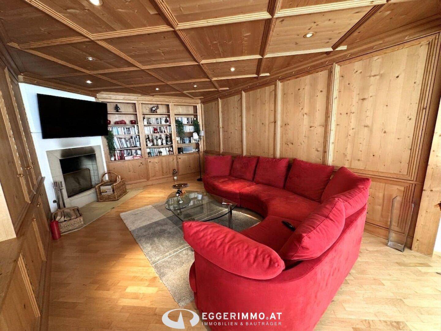 Wohnzimmer mit traditioneller Holzverkleidung an Wänden und Decke, rotem Rundsofa und Kamin.