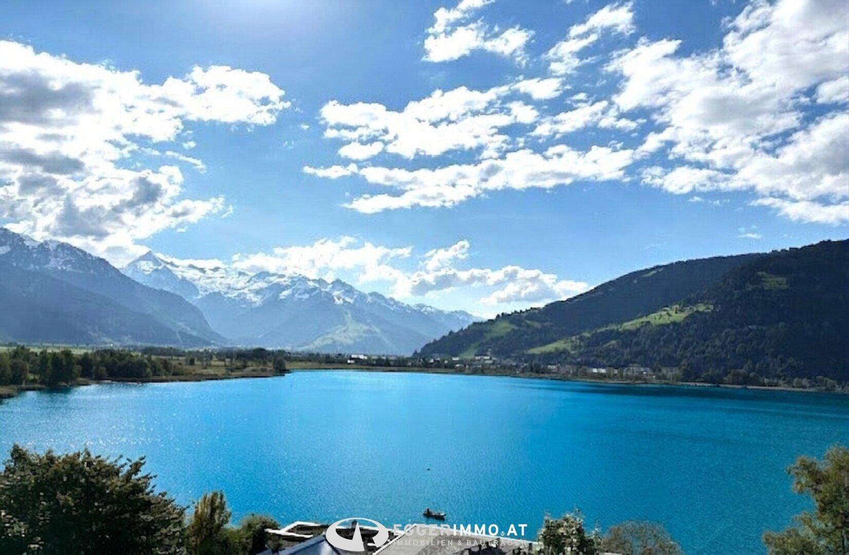 Weitläufiger Panoramablick auf einen türkisblauen See, umgeben von majestätischen Bergen unter einem bewölkten Himmel.
