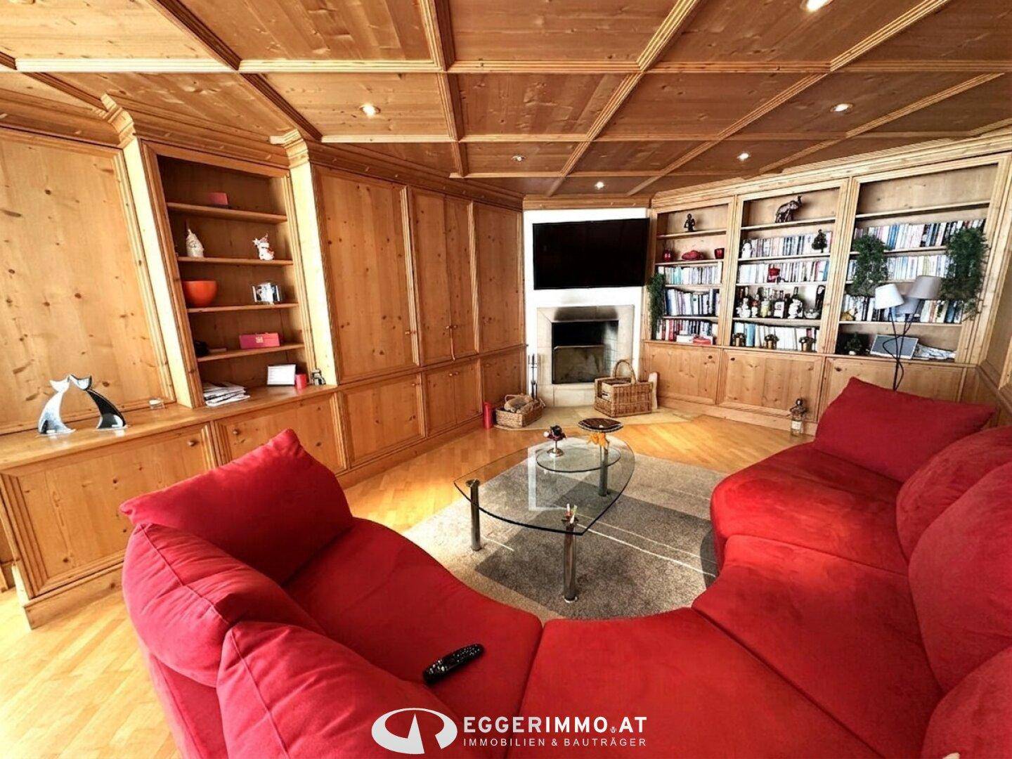 Gemütliches Wohnzimmer im alpinen Stil mit viel Holzvertäfelung, rotem Sofa und integrierten Bücherregalen.