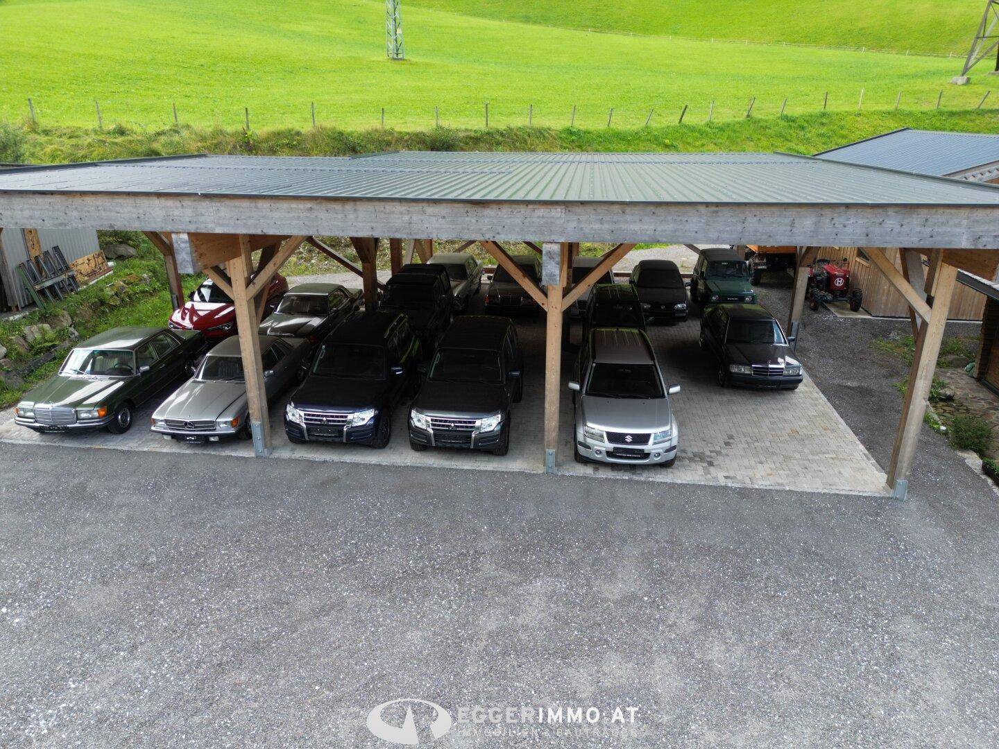Geräumiger Carport mit Holzbalken, bietet Platz für mehrere Fahrzeuge auf dem Schotterplatz.