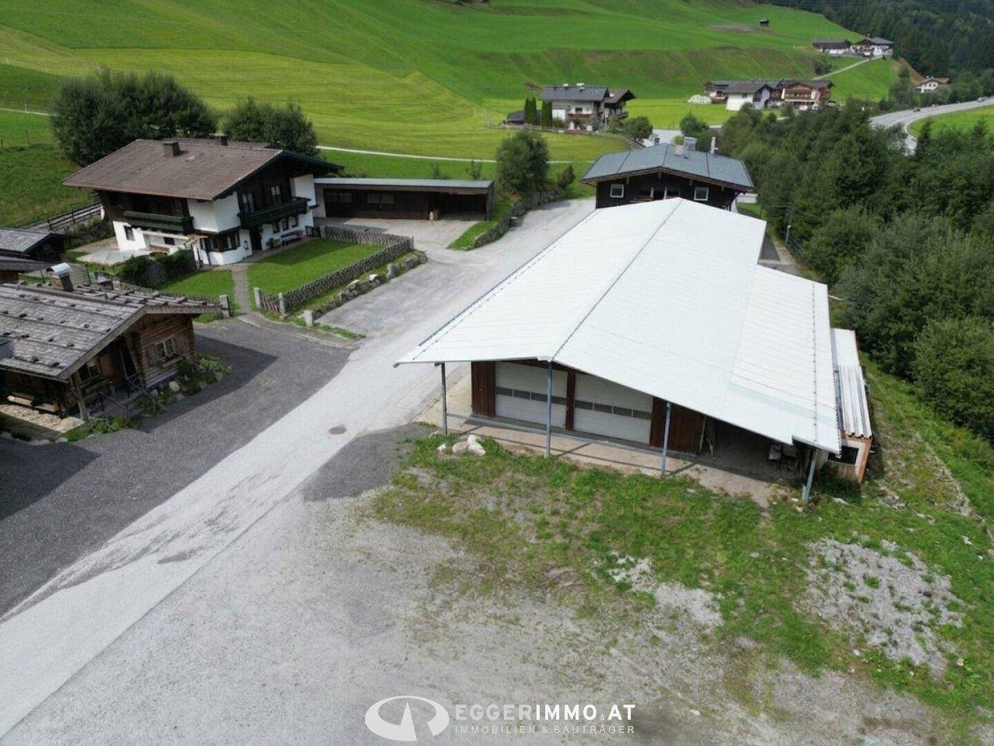 Luftaufnahme eines Gewerbegebäudes mit großem Dach und einem traditionellen Wohnhaus im Hintergrund.