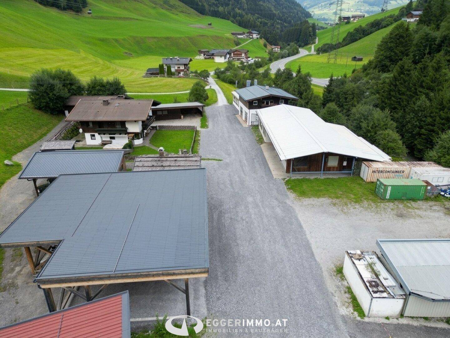 Überblick über mehrere Gebäude und eine Schotterstraße in einer ländlichen Umgebung mit viel Grün.